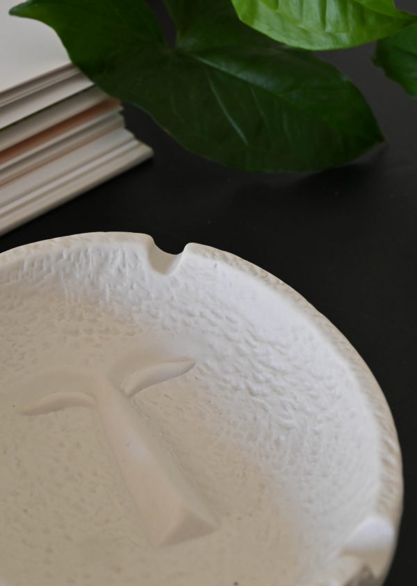 Cenicero de cerámica blanco con relieve de un rostro.