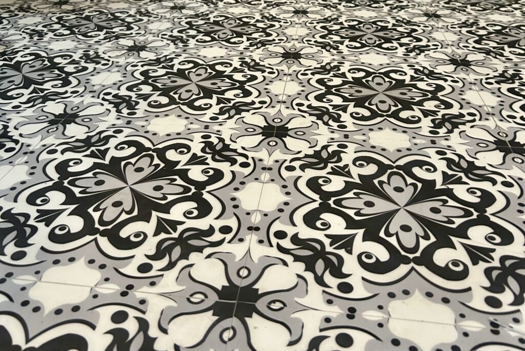 La imagen muestra baldosas adhesivas instaladas en un piso. Las baldosas son blancas con negro.